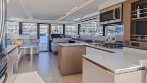 A modern kitchen with a central island, built-in appliances, and large windows offering views of the marina and buildings. - Caribbean Dream: Sun-soaked Sailing Adventure from Bahamas to Islas Abaco (Marsh Harbour)
