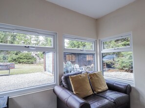 Una habitación con sofá de cuero, dos ventanas y vista a un patio trasero.