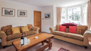 A living room with two patterned sofas, a wooden coffee table, and a window with curtains. - Achnagonlin House (Grantown-on-Spey)