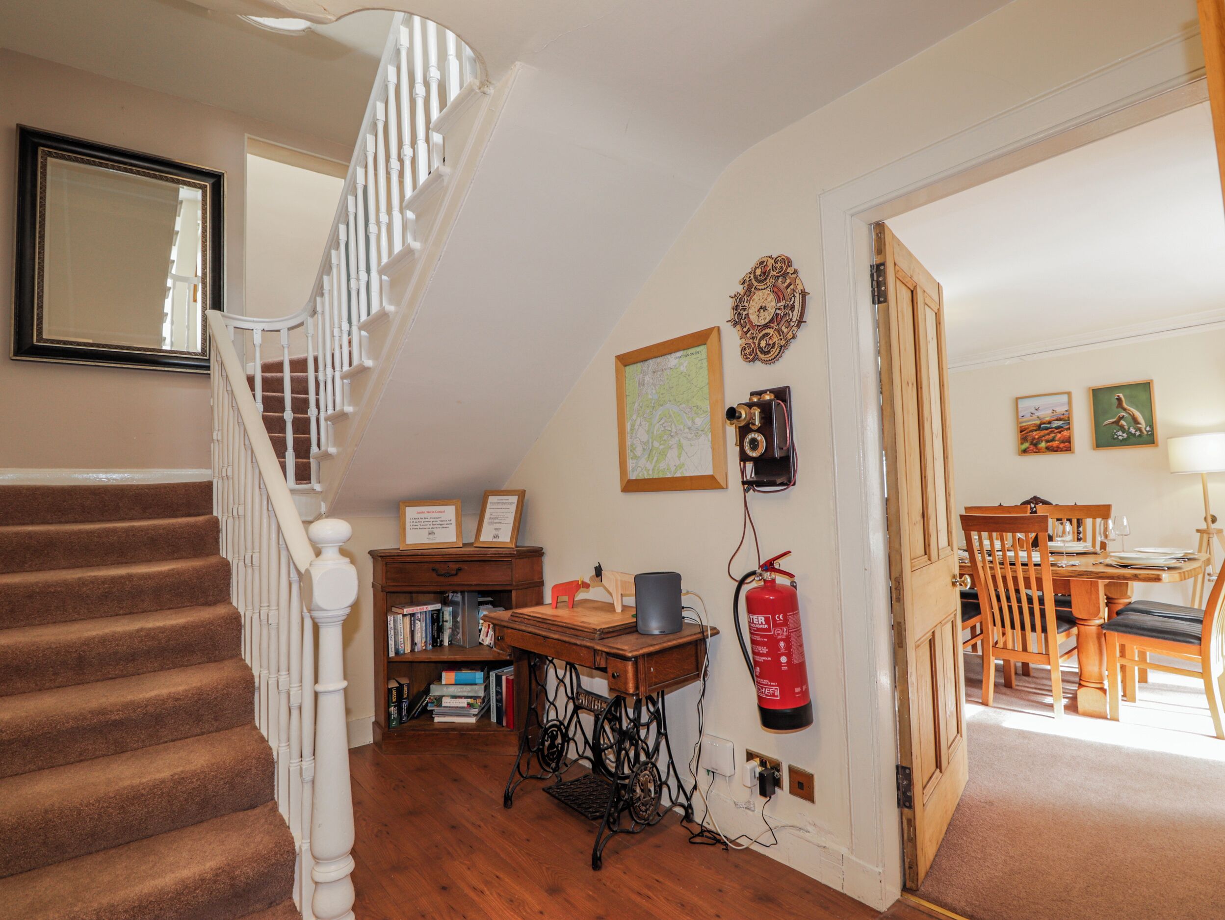 A staircase with a white railing, a bookshelf, a vintage camera, and a fire extinguisher mounted on the wall.