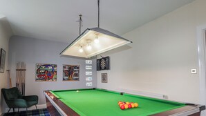 A pool table with a green felt surface, a pool cue, and a set of billiard balls. There is a green chair and a plaid-patterned floor. - Achnagonlin House (Grantown-on-Spey)