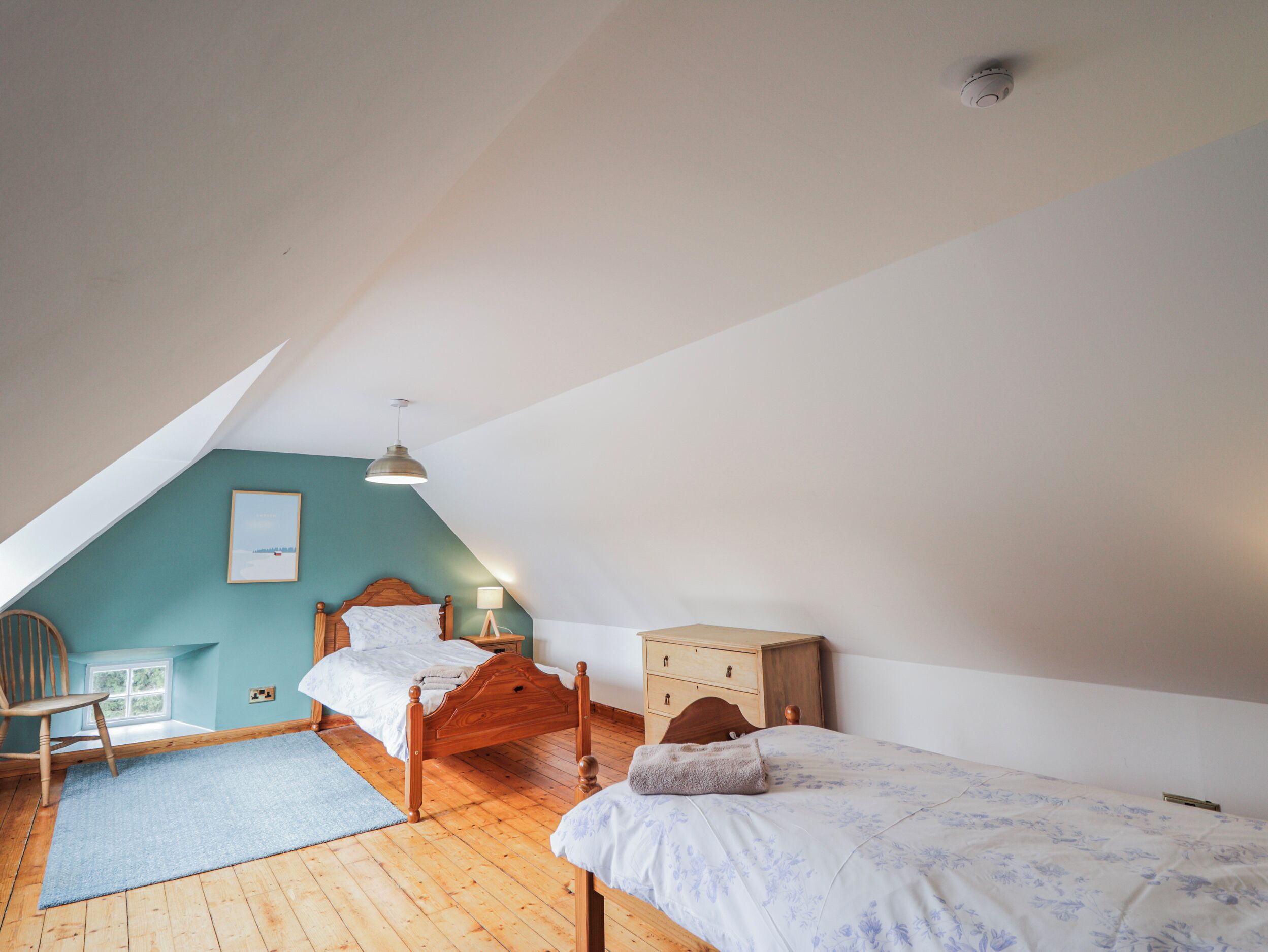 A bedroom with a sloped ceiling, a wooden bed, a nightstand, a chair, and a small wooden cabinet.