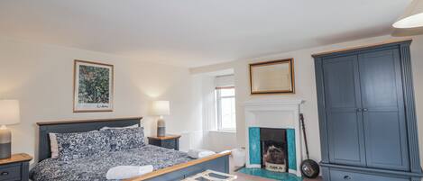 A bedroom with a bed, bedside tables, a fireplace, a wardrobe, and a framed picture on the wall.
