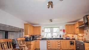 A kitchen with wooden cabinets, a central island, a stove, and a dining area with chairs. - Achnagonlin House (Grantown-on-Spey)