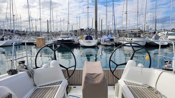 A marina with multiple boats docked, a clear sky, and a wooden deck with two chairs.