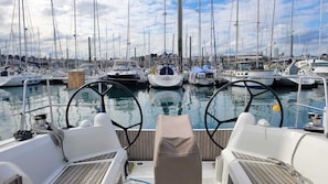 A marina with multiple boats docked, a clear sky, and a wooden deck with two chairs.