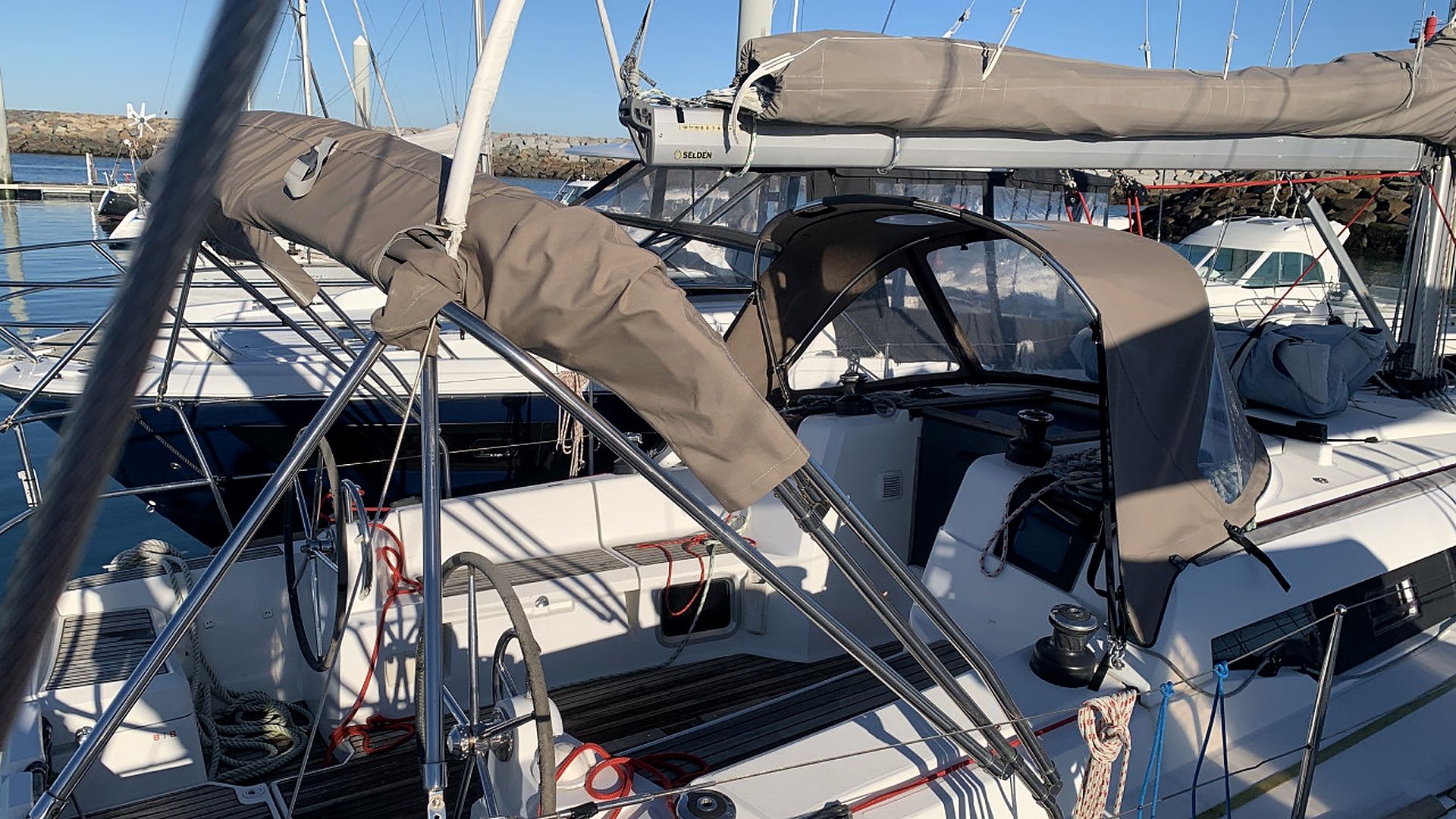 Un voilier est amarré dans une marina, avec un pont partiellement couvert, un gréement visible et un treuil.
