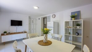 A modern kitchen with white cabinetry, a flat-screen TV mounted above the counter, a dining table with chairs, and a white shelving unit with decorative items. - Vacation apartment close to the beach in a quiet location in Crikvenica-Dramalj (Dramalj)