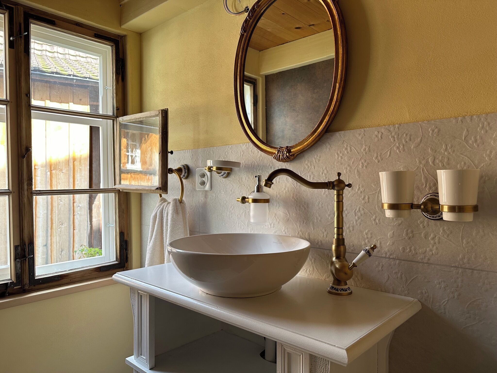 A bathroom with a large vessel sink, a mirror, a towel rack, and a window with a view of a wooden fence.
