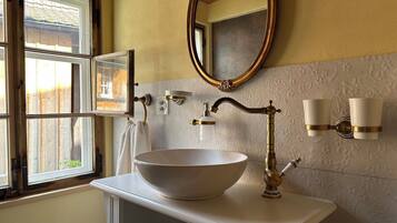 A bathroom with a large vessel sink, a mirror, a towel rack, and a window with a view of a wooden fence.