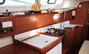 A compact kitchen with wooden cabinets, a white sink, and a stove. - Sun-Kissed Sailing to Costa Esmeralda: A Beach Lover's Dream (Saint-Quay-Portrieux)