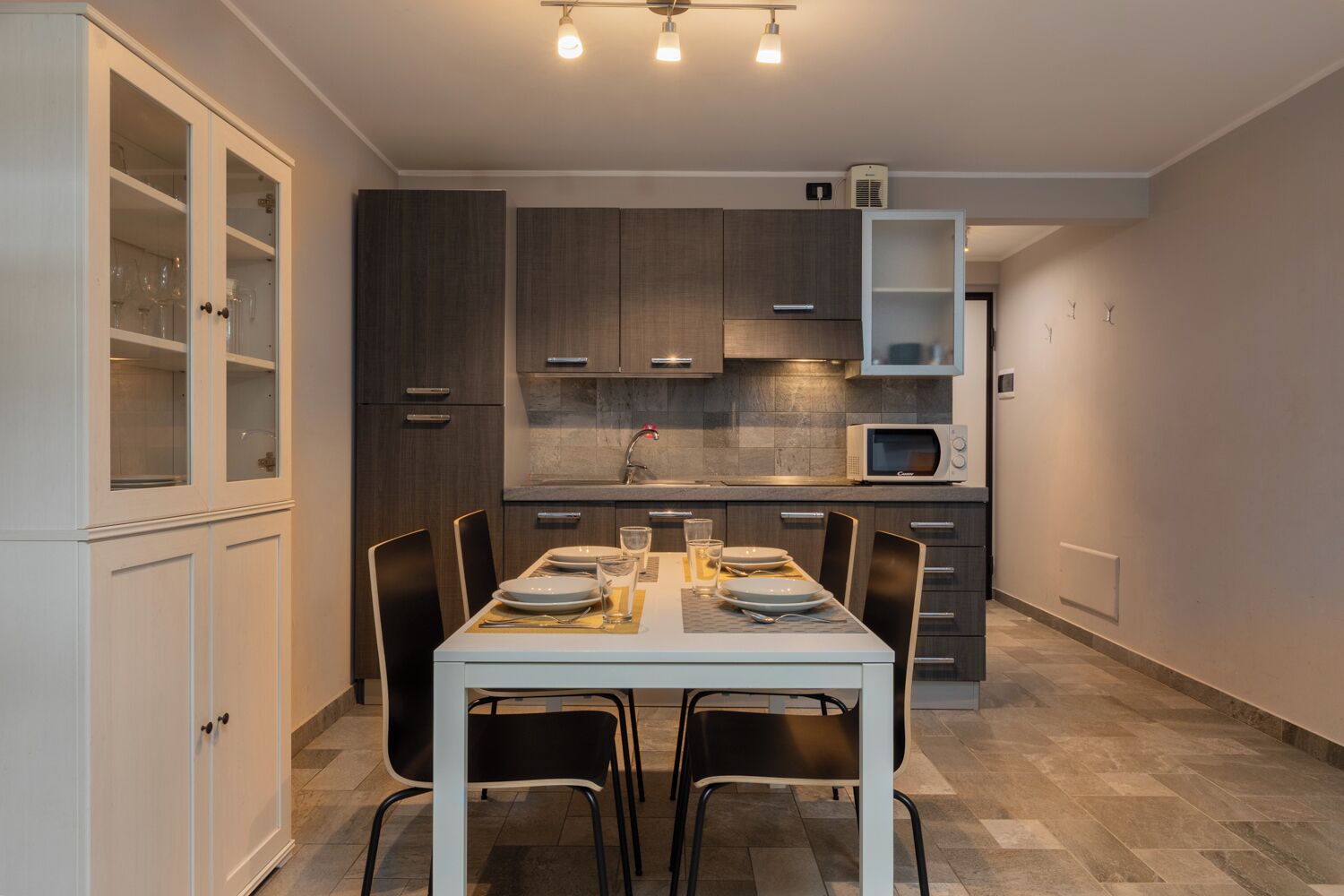 A modern kitchen with dark wood cabinets, a white dining table set for four, and a microwave above it.