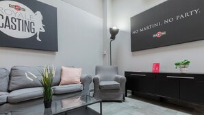 Ein moderner Loungebereich mit grauem Sofa, einem schwarzen Couchtisch, einem grauen Sessel und einem schwarzen Schrank mit einem roten Schild.