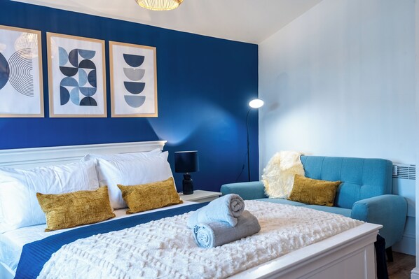 A hotel room with a bed, a blue sofa, and three framed artworks on the wall.
