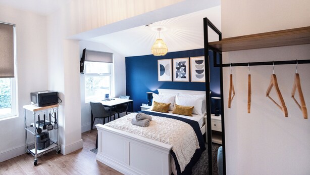A bedroom with a bed, bedside table, lamp, and a desk with a chair. - Glan Neigr by Guestz (Rhosneigr)