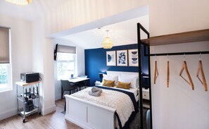 A bedroom with a bed, bedside table, lamp, and a desk with a chair.