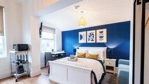 A modern bedroom with a white bed, blue accent walls, a desk, and a television on a shelf. - Glan Neigr by Guestz (Rhosneigr)