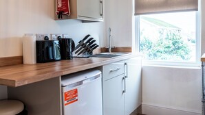 A kitchen with a microwave, toaster, and knives on the counter, a sink, and a window with a view of greenery. - Glan Neigr by Guestz (Rhosneigr)