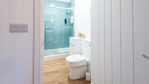 A modern bathroom with a glass shower enclosure, a white toilet, and a wooden floor. - Glan Neigr by Guestz (Rhosneigr)