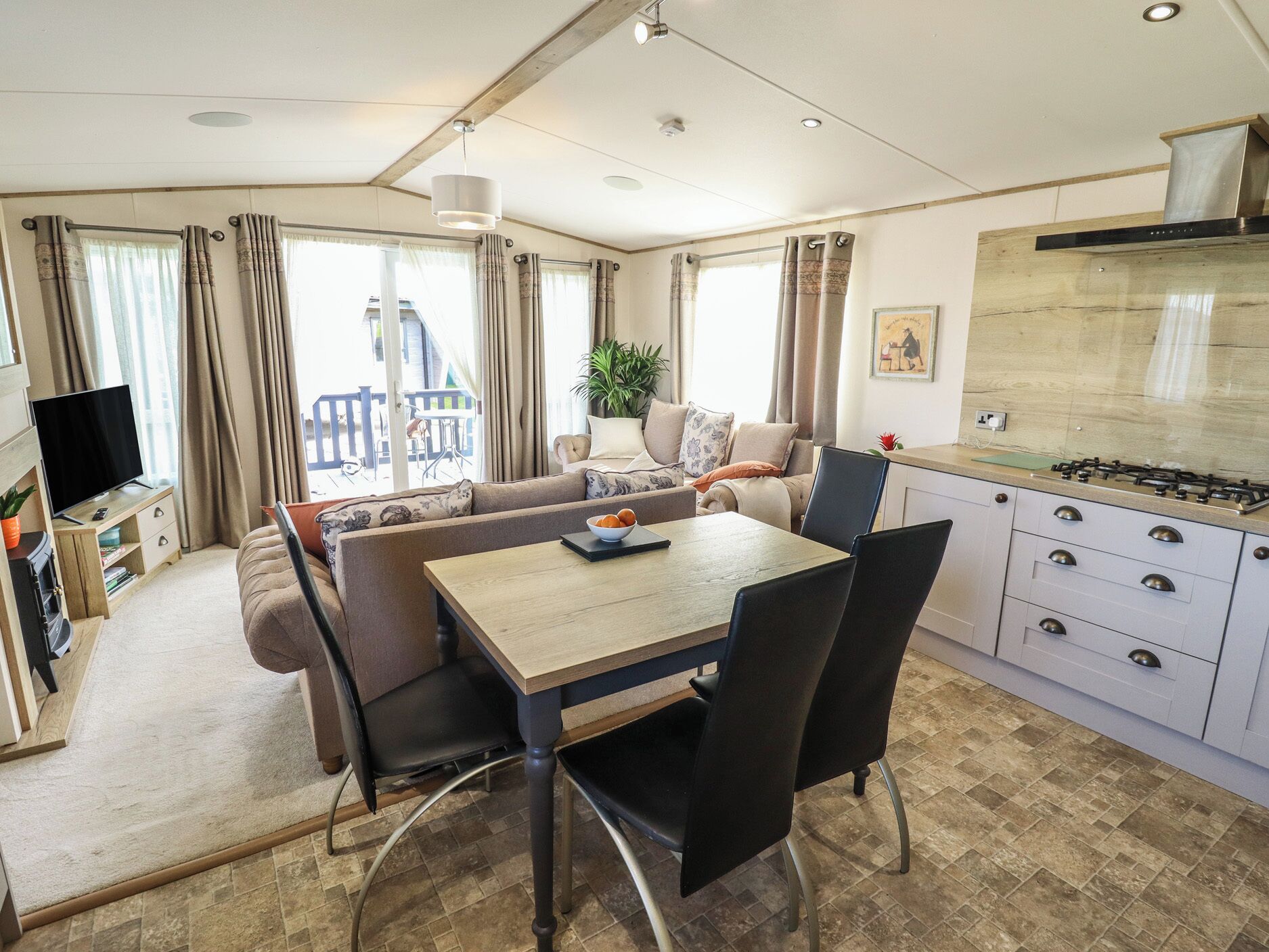 A modern kitchen with a gas stove, dining table with chairs, and a sofa in a bright room with large windows.