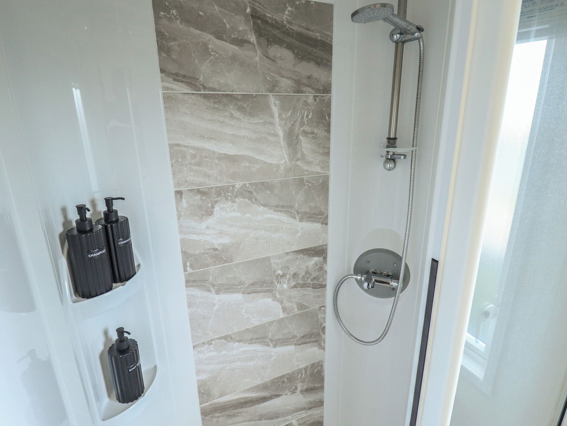 A bathroom with a shower, marble walls, and toiletries.