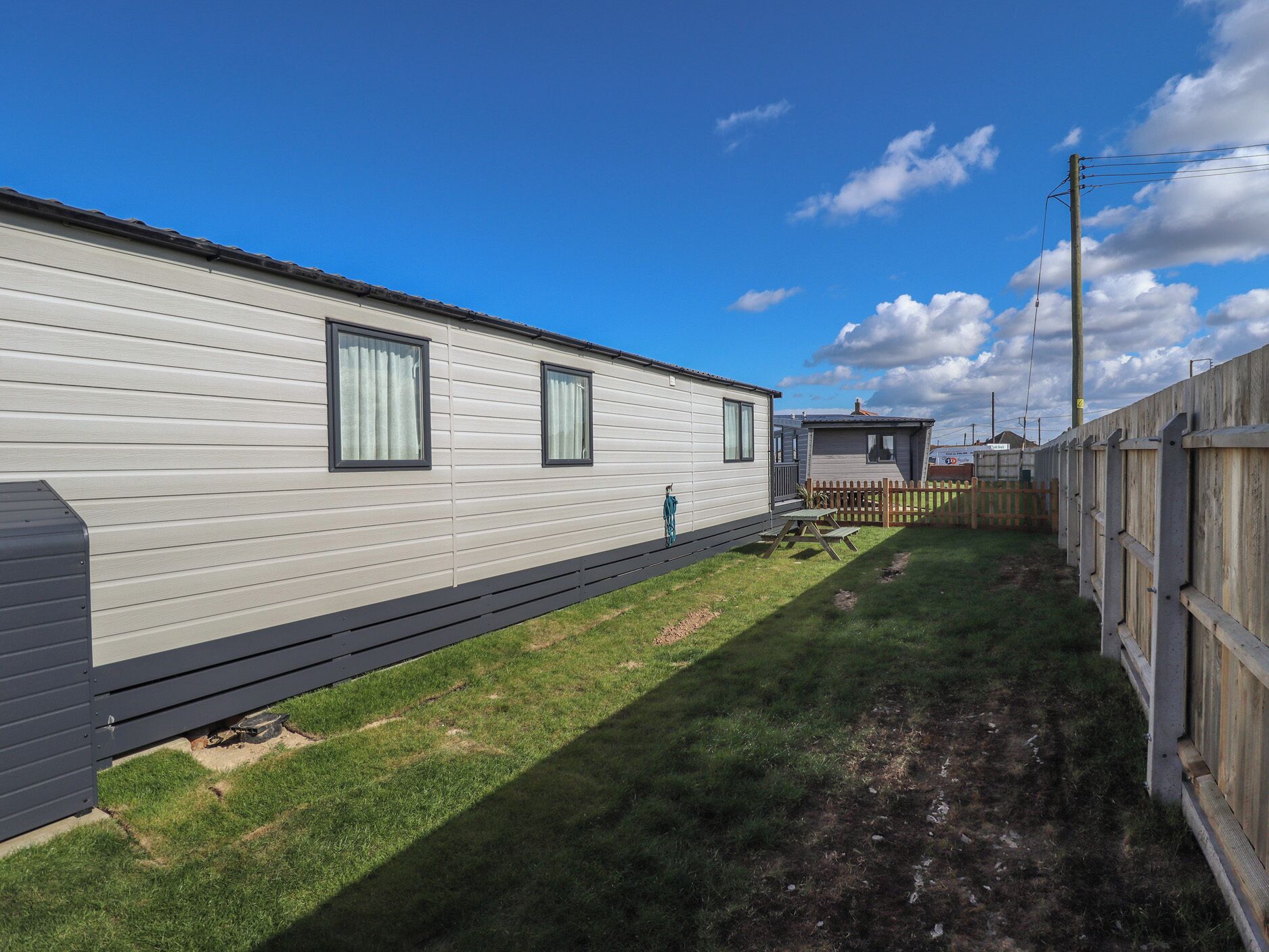 A mobile home with a deck, a fenced yard, and a clear sky.