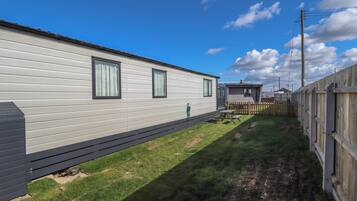A mobile home with a deck, a fenced yard, and a clear sky.