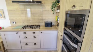 Une cuisine compacte équipée d’une cuisinière à gaz, d’un four à micro-ondes et d’un four traditionnel, de meubles en bois et d’un pare-feu en carreaux.