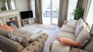 Un salon comprenant un ensemble de canapés, un téléviseur à écran plat, une cheminée et une vue sur l’extérieur.