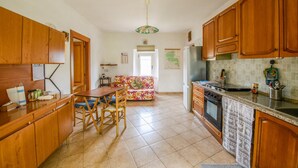 A kitchen with wooden cabinets, a dining table with chairs, a refrigerator, and a stove. - Phoebe House - Capestrano (Capestrano)