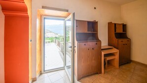 A room with a sliding glass door leading to a balcony, wooden furniture, and a tiled floor. - Phoebe House - Capestrano (Capestrano)
