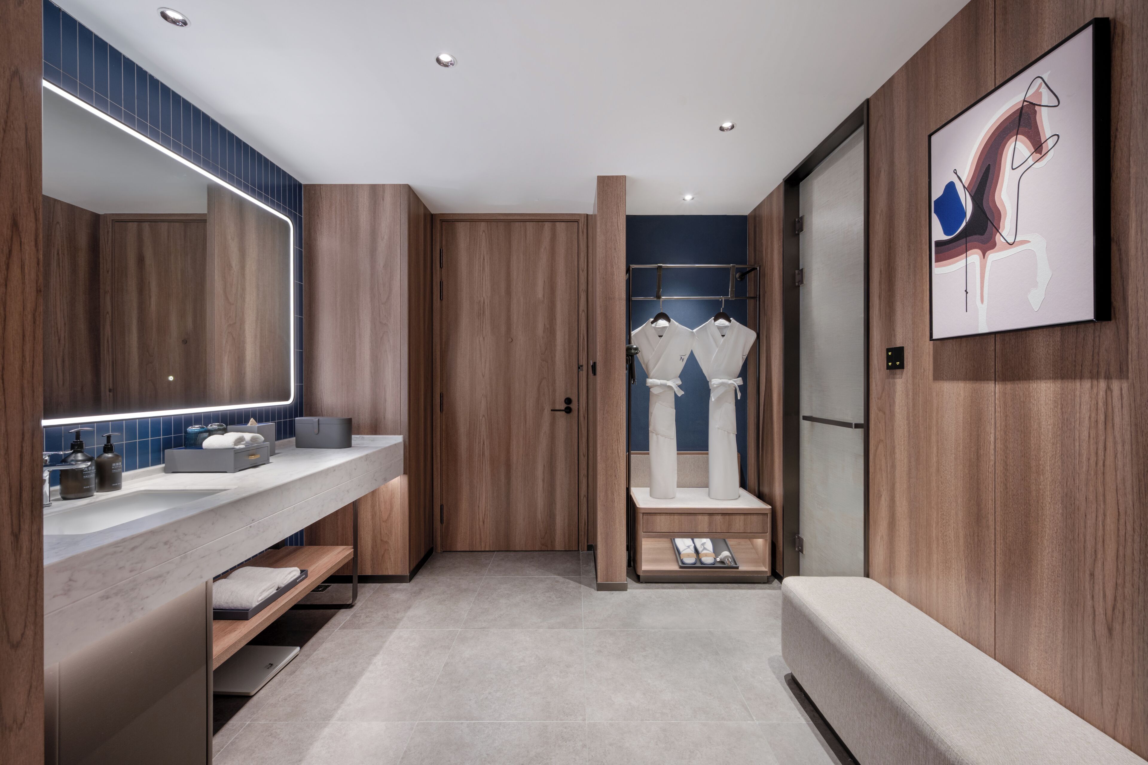 A modern bathroom with wooden paneling, a large mirror, dual sinks, and a bench.