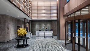 Un hall con mostrador de recepción, dos empleados, un jarrón con flores amarillas, un suelo estampado y un diseño de techo moderno.