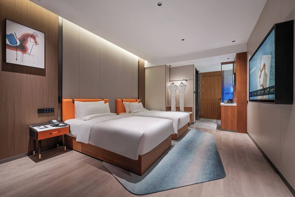 A modern hotel room with a large bed, bedside tables, a flat-screen TV, and a wardrobe.