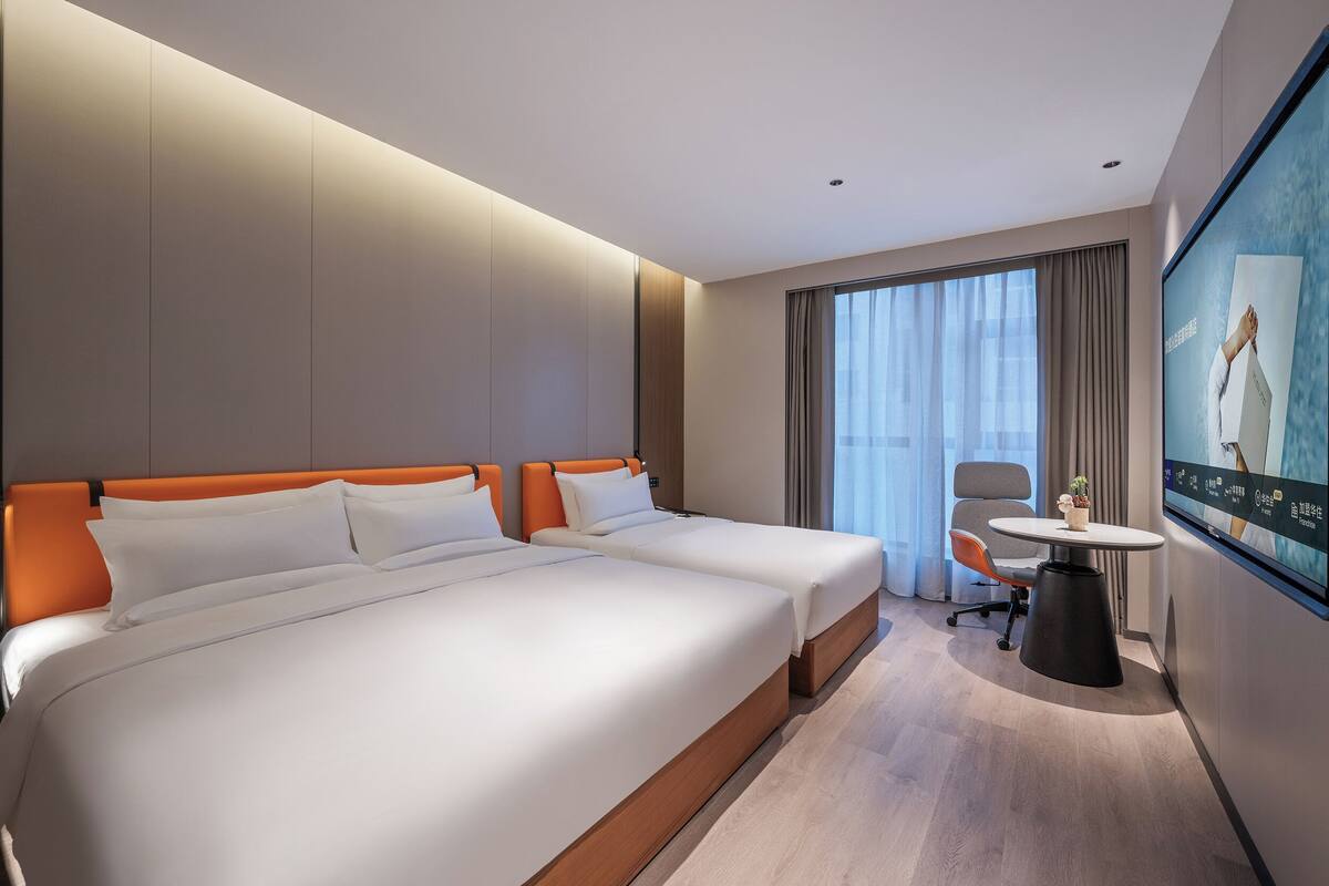 A hotel room with two beds, a desk, a chair, and a large TV screen.
