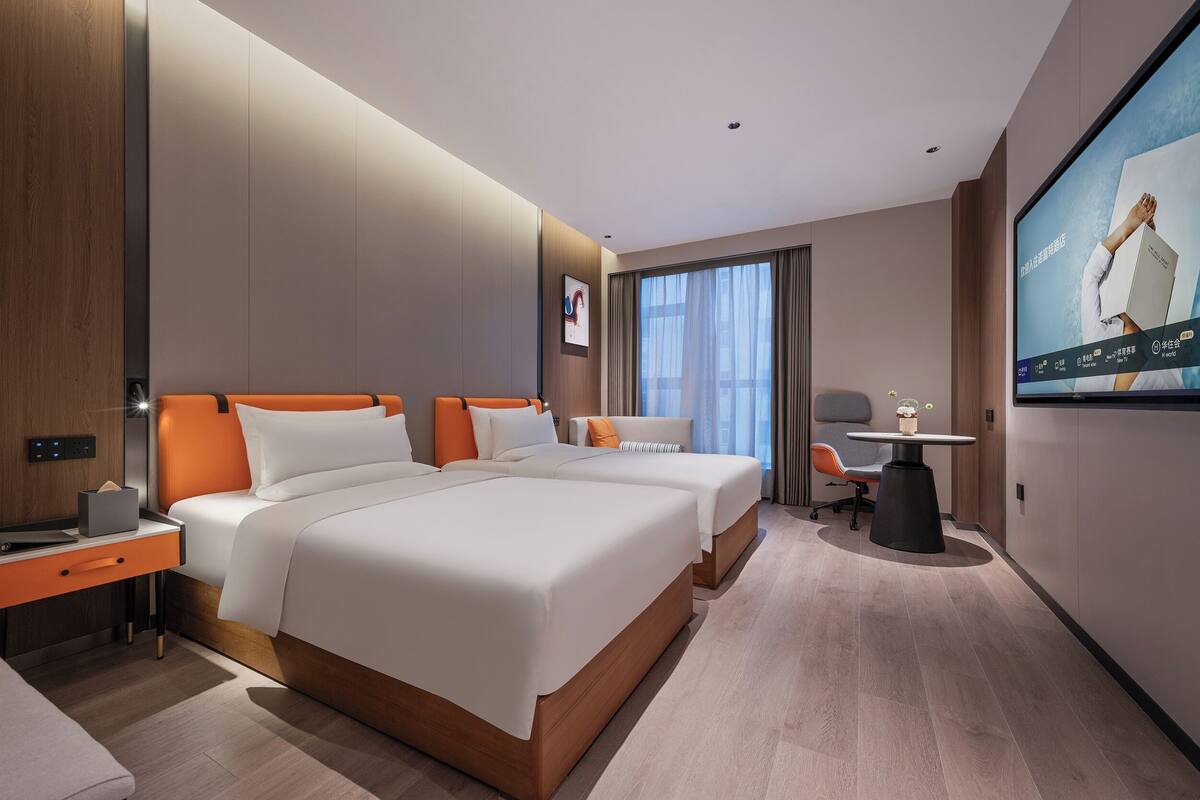 A hotel room with two beds, a desk, a chair, a TV, and a window with curtains.