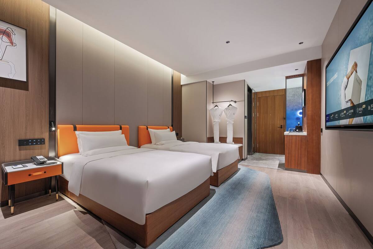 A hotel room with two beds, a nightstand, a TV, and a large mirror.