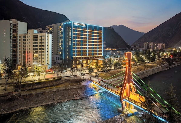 A hotel with a modern design, a prominent sign, and a view of a river and mountains.