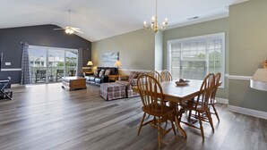 A spacious living area with a dining table, wooden chairs, a sofa, and a ceiling fan. - Magnolia North 305 (Myrtle Beach)
