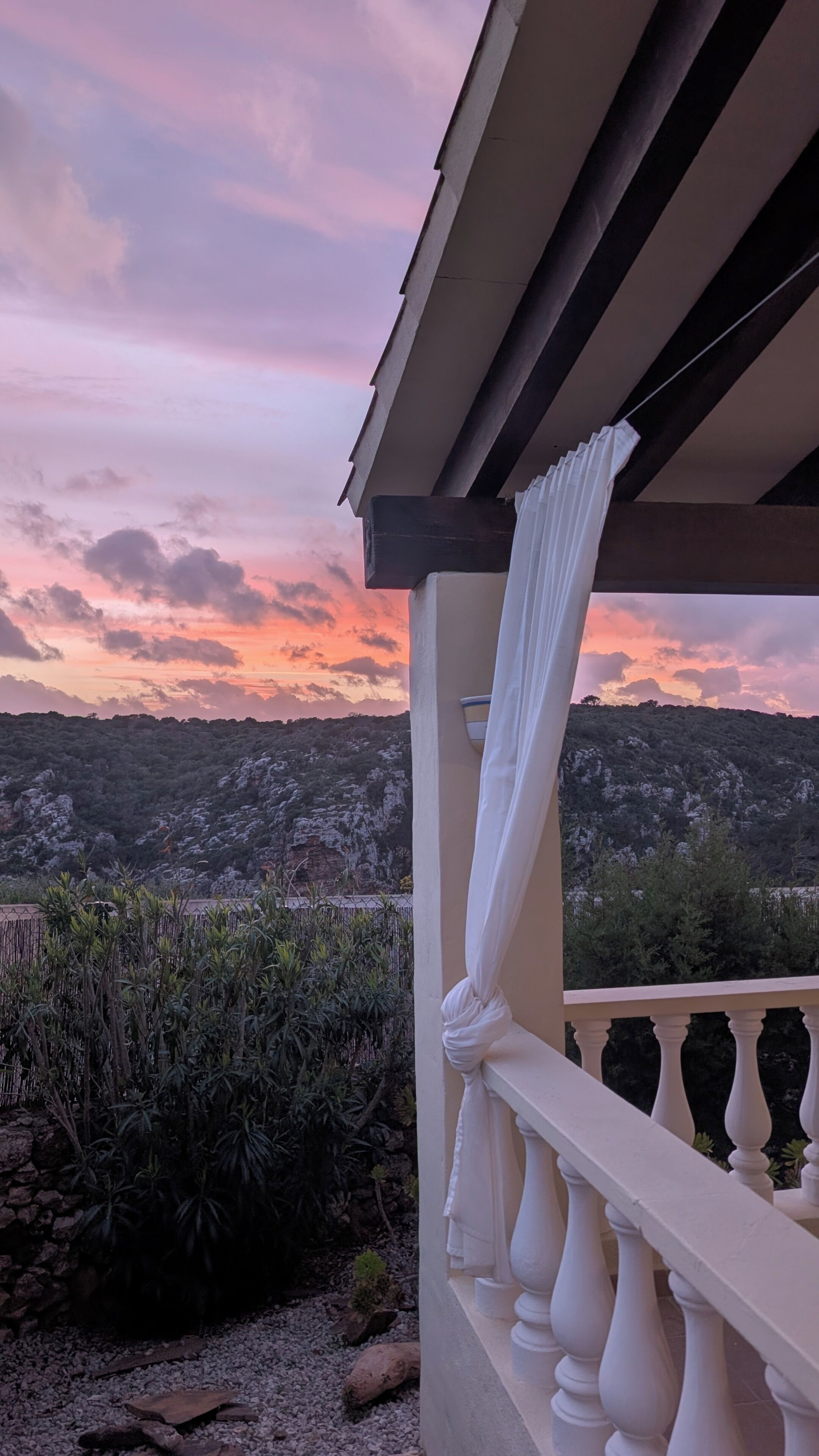 Een balkon met uitzicht op een glooiend landschap tijdens zonsondergang.