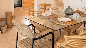 A dining area with a glass table, wicker chairs, and a kitchen in the background. - Menorcan house with private pool, sea views, 10 minutes from the beach. (Cala en Porter)