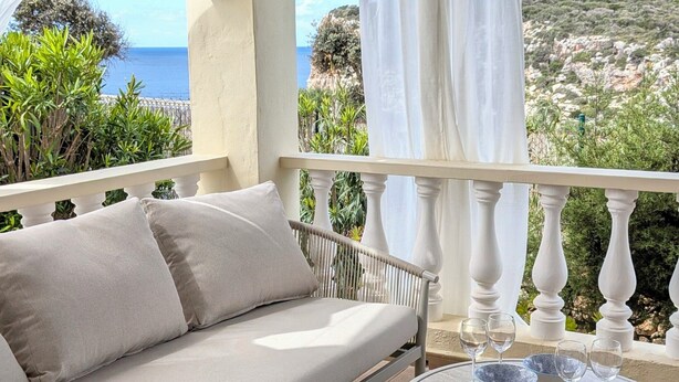 A balcony with a sofa, a round table with glasses and bowls, and a view of the sea. - Menorcan house with private pool, sea views, 10 minutes from the beach. (Cala en Porter)