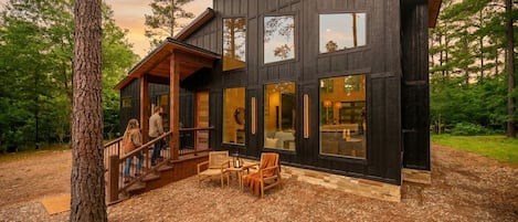 Una cabaña moderna de madera con terraza, ventanas amplias y mobiliario exterior.