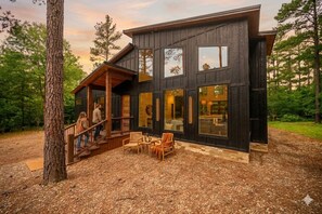 Una moderna baita di legno con veranda, ampie finestre e posti a sedere all'aperto.