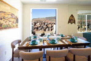 A dining area with a table set for four, chairs, a painting on the wall, and a view of a rocky landscape through an open door. - Southern Utah Wonder... Under the Sage Arches. Your family will be close to everything from parks to town when you stay at this centrally-located house. (Washington)