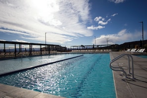 A swimming pool with clear water, surrounded by lounge chairs and a metal railing.