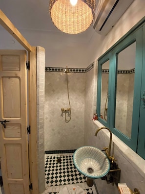 A bathroom with a checkered floor, a blue and white sink, a gold showerhead, and a teal-framed mirror. - Luxurious 5-bedroom Apartment in Marrakesh With Full Accessibility (Marrakech)