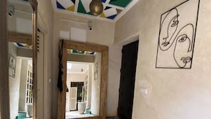 A hallway with a geometric patterned floor, a ceiling with a light fixture, and a wall with a minimalist face painting. - Luxurious 5-bedroom Apartment in Marrakesh With Full Accessibility (Marrakech)