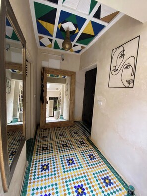A hallway with a geometric patterned floor, a ceiling with a light fixture, and a wall with a minimalist face painting. - Luxurious 5-bedroom Apartment in Marrakesh With Full Accessibility (Marrakech)