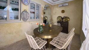 A dining area with a round table, white wicker chairs, a decorative mirror, and wall-mounted plates. - Luxurious 5-bedroom Apartment in Marrakesh With Full Accessibility (Marrakech)